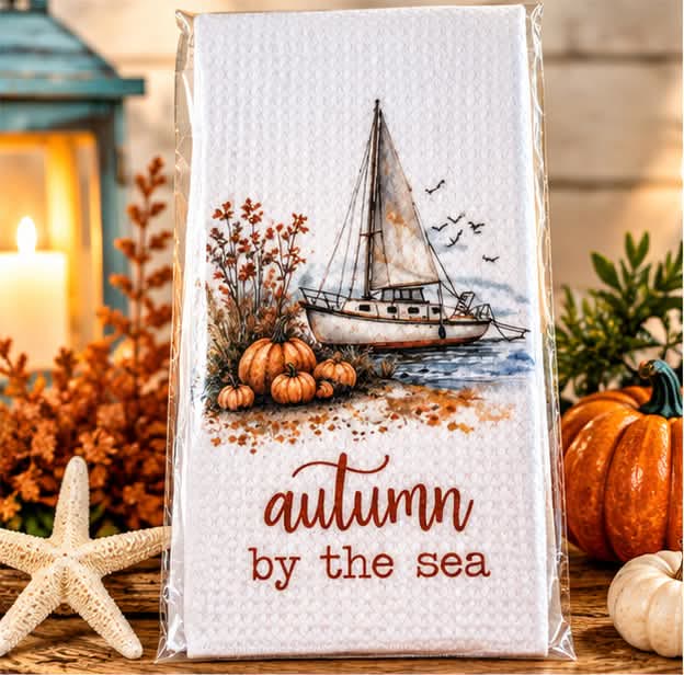 Waffle kitchen towel printed with a sailboat, pumpkins and the words autumn by the sea