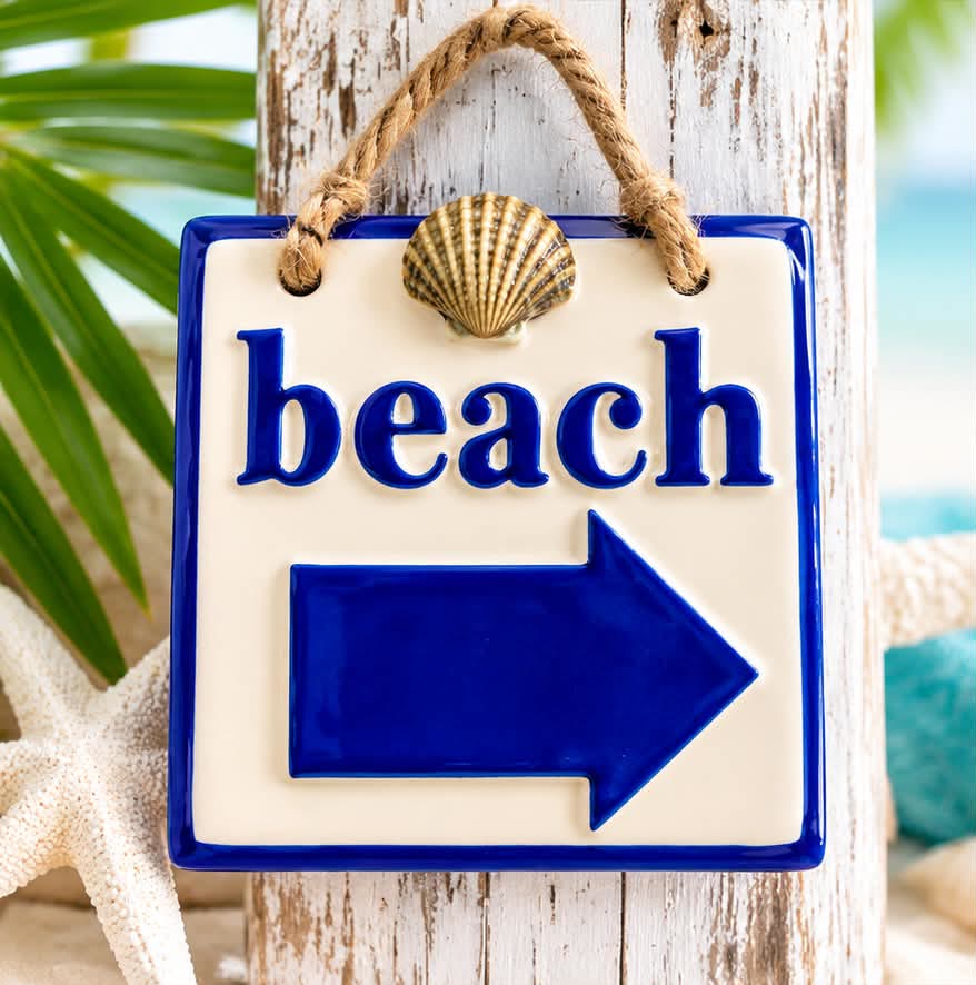 Small ceramic sign reading beach with a blue arrow, hung from a rope with a seashell