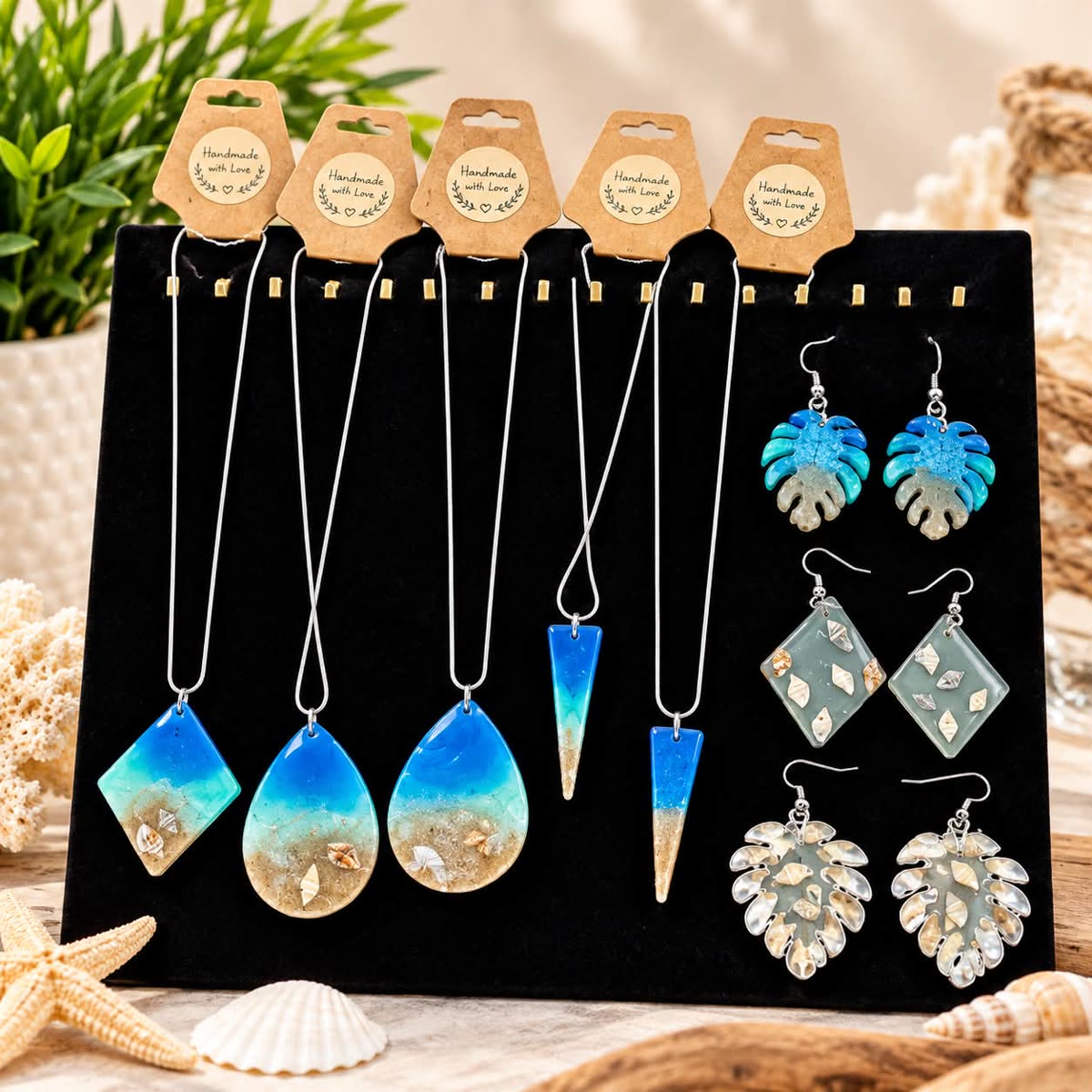 Display of blue resin pendant necklaces with sand and shells, plus monstera leaf and diamond-shaped resin earrings